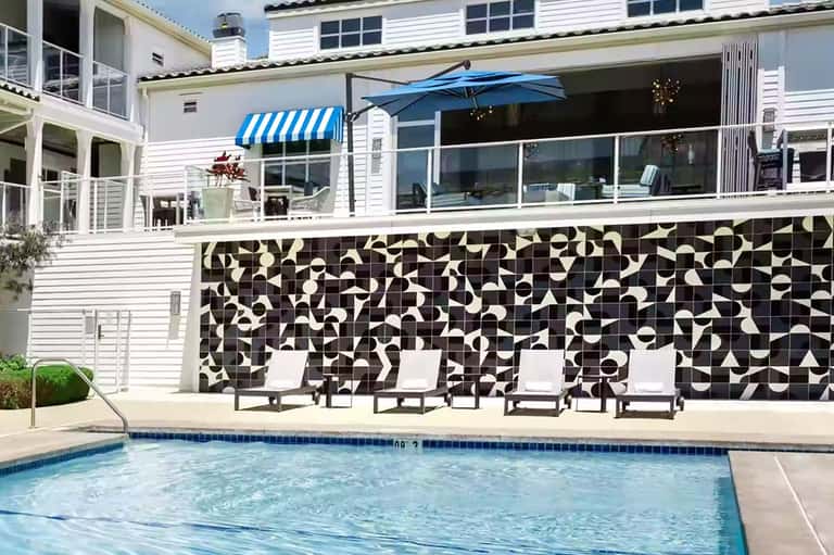 Modern beach house with white exterior, black and white tile wall, pool and blue umbrella