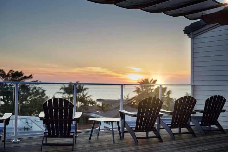 Rooftop deck with Adirondack chairs, sunset ocean view, and architectural structure at dusk