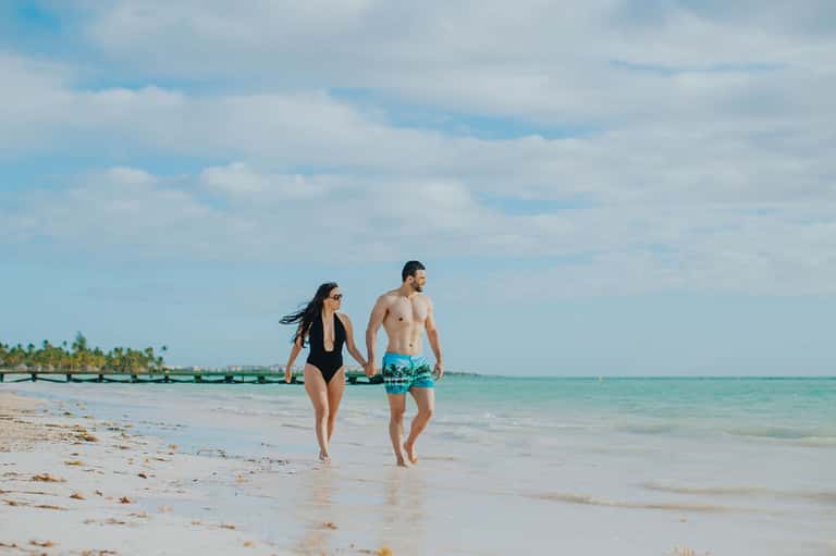 Couple walking hand-in-hand on sandy beach with clear turquoise water and tropical scenery