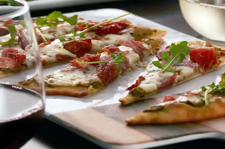 Gourmet appetizers on white plate with prosciutto, cheese, and fresh herb garnish