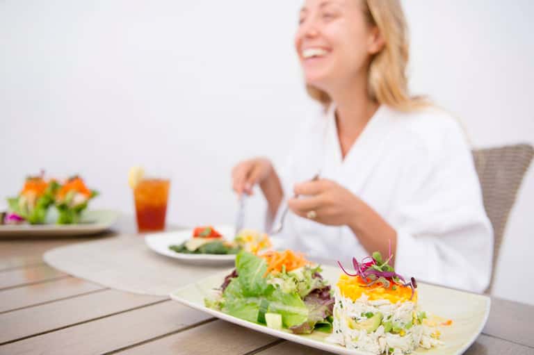 Woman dining outdoors with colorful salad plate and tropical beverage at resort restaurant