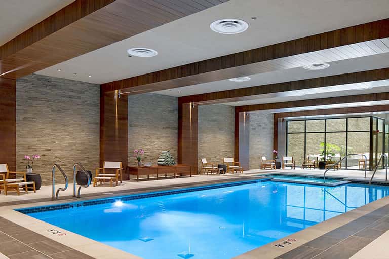 Indoor heated swimming pool with wooden beams, large windows, and comfortable seating area