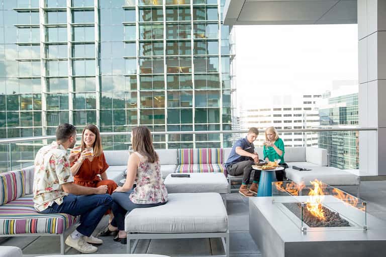 High-rise rooftop lounge with guests, fire pit, and panoramic city skyline views