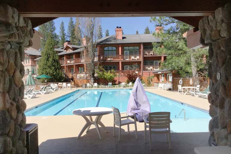 Resort lap pool framed by stone archway with mountain lodges and lounge seating visible