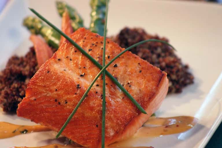 Gourmet plated salmon dish with fresh greens and sauce on white plate, fine dining presentation