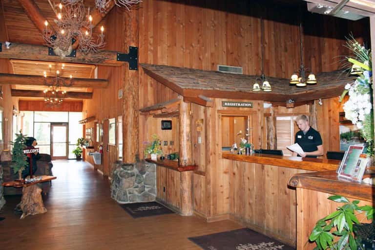 Rustic lodge lobby with wooden beams, chandeliers, and registration desk