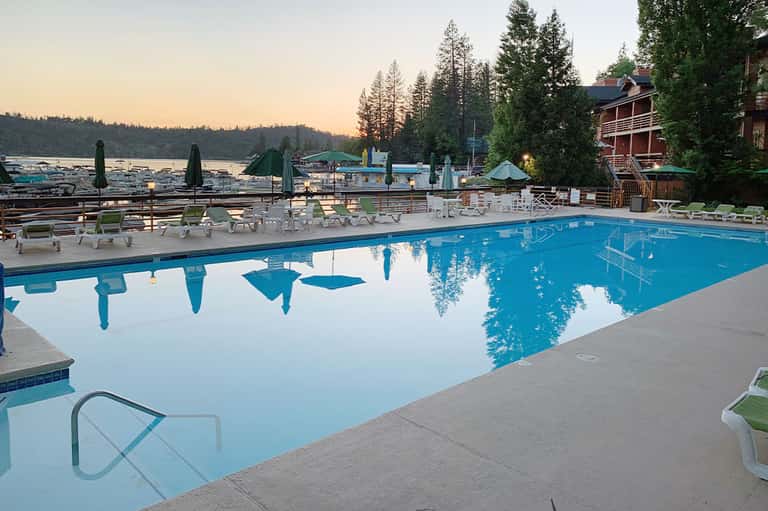 Large resort pool at dusk reflecting trees and lodge building with Adirondack chairs lakeside