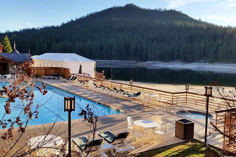 Lakeside resort pool with forest mountains and wooden dock overlooking pristine water
