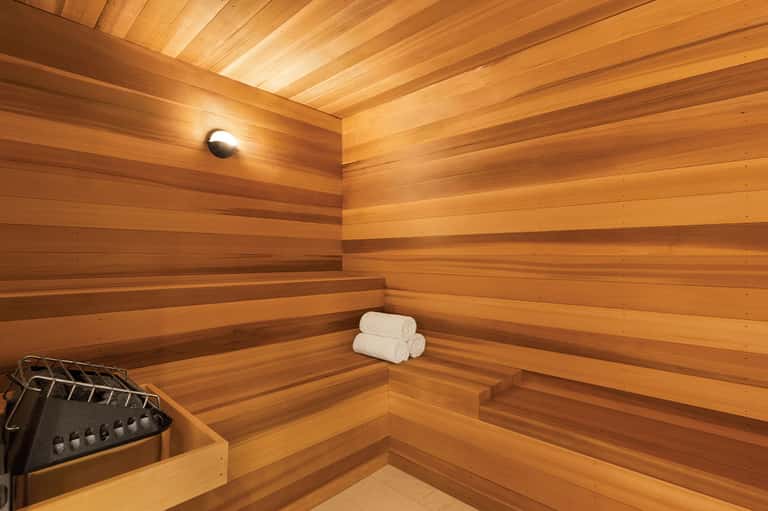 Wooden sauna interior with tiered benches, cedar walls, rolled white towels, and ambient lighting