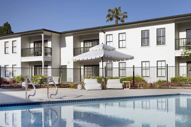 Modern white pool cabanas with lounge seating, white umbrella, and residential-style buildings