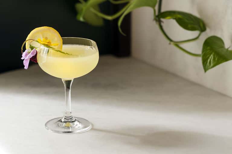 Elegant cocktail with lemon slice and purple flower garnish on marble surface