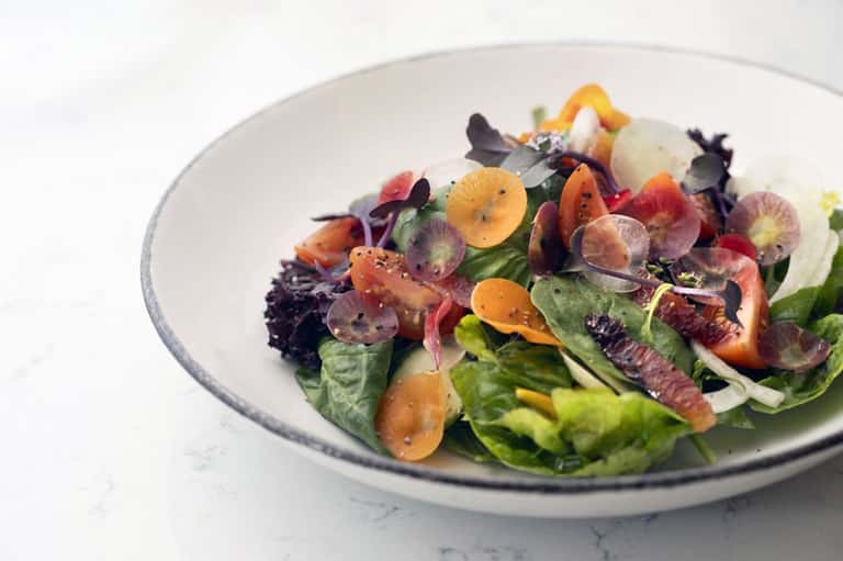 Artfully plated salad with microgreens and edible flowers on white plate