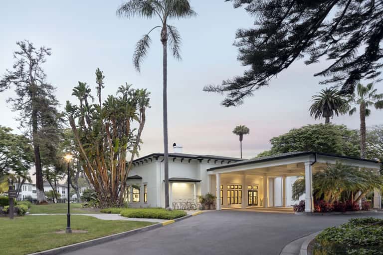 Modern white resort building entrance at dusk with palm trees and landscaping