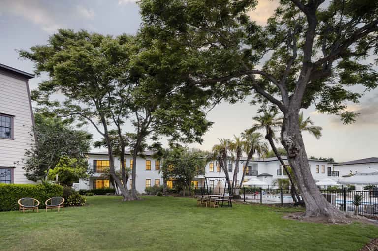 Resort courtyard with mature trees, white buildings, and green lawn at dusk