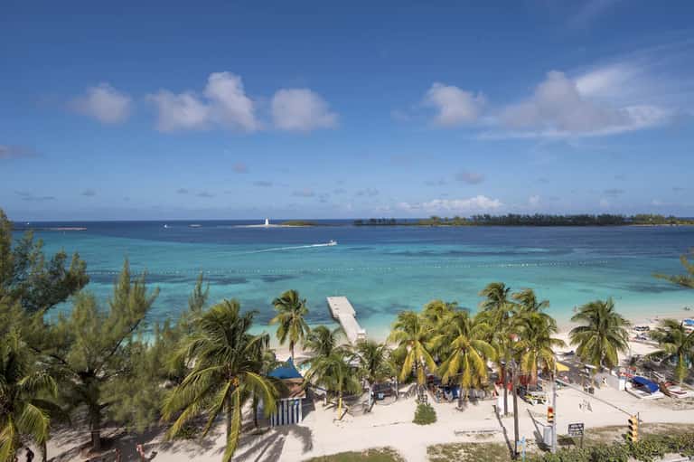 Tropical beach resort with palm trees, turquoise waters, white sand, and anchored boat