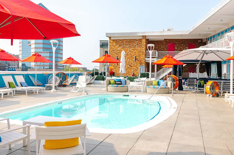 Resort pool deck with bright red and orange umbrellas, loungers, colorful play areas, and contemporary architecture