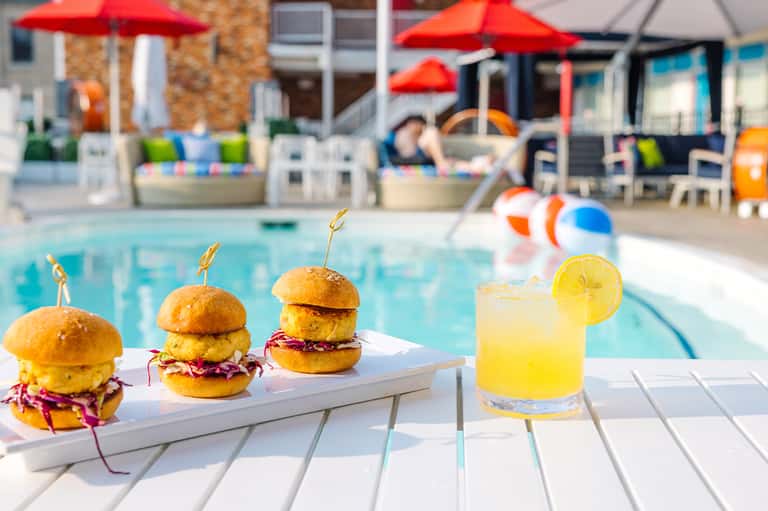 Gourmet sliders and cocktail by resort pool with red umbrellas, loungers, and red umbrellas