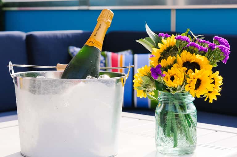 Champagne bottle in ice bucket with sunflowers and purple flowers on blue lounge background