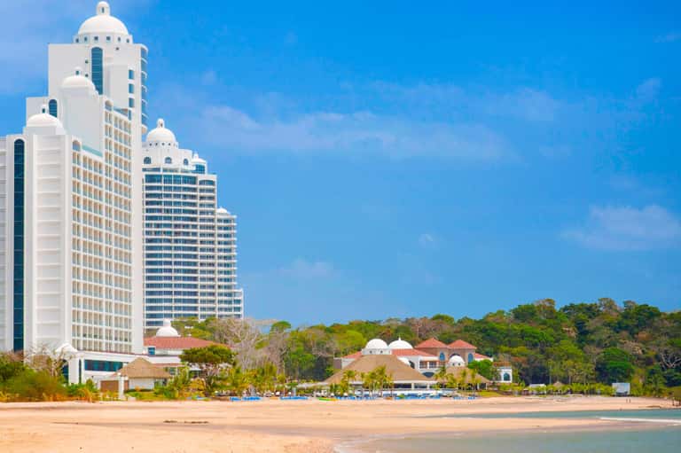 White high-rise resort buildings overlooking a sandy beach with turquoise water and palm trees