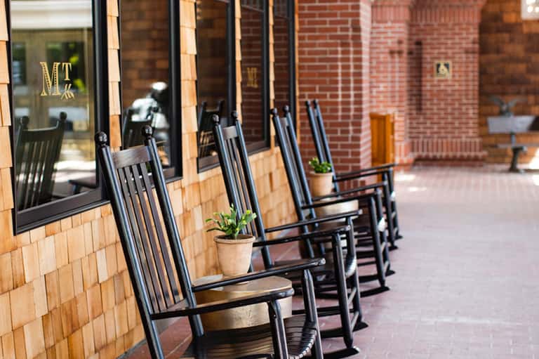 Row of black rocking chairs on brick patio outside historic building with windows