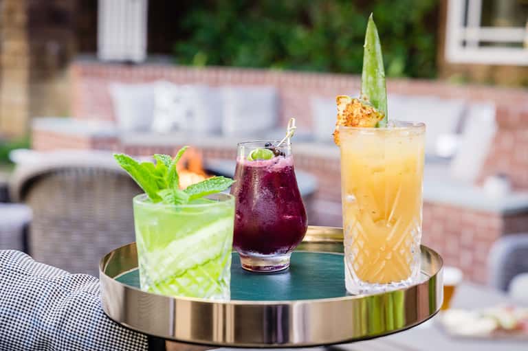 Three cocktails on tray with mint and pineapple garnishes poolside