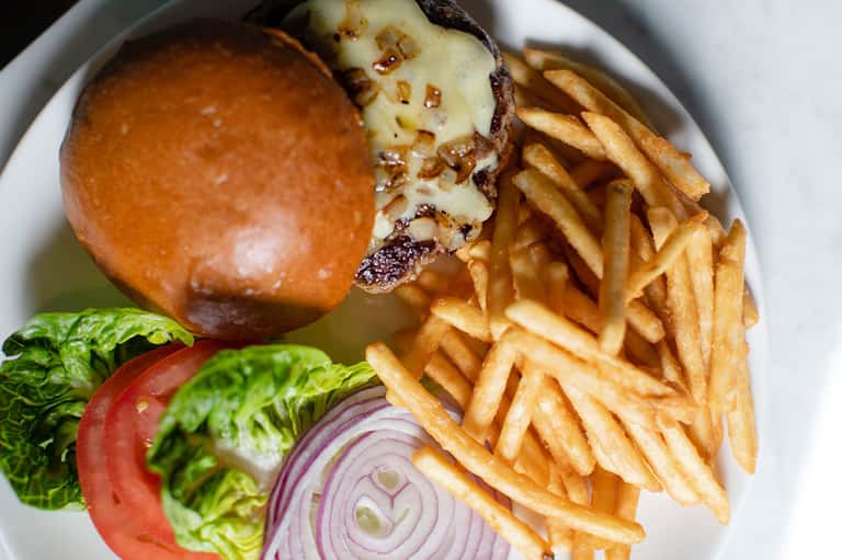 Gourmet cheeseburger with melted cheese and fries on a white plate