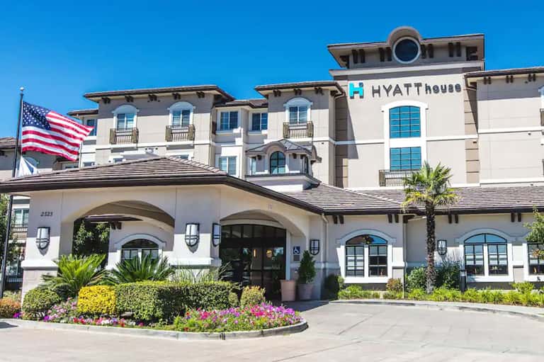 White Hyatt House hotel exterior with American flag, manicured landscaping, and palm trees