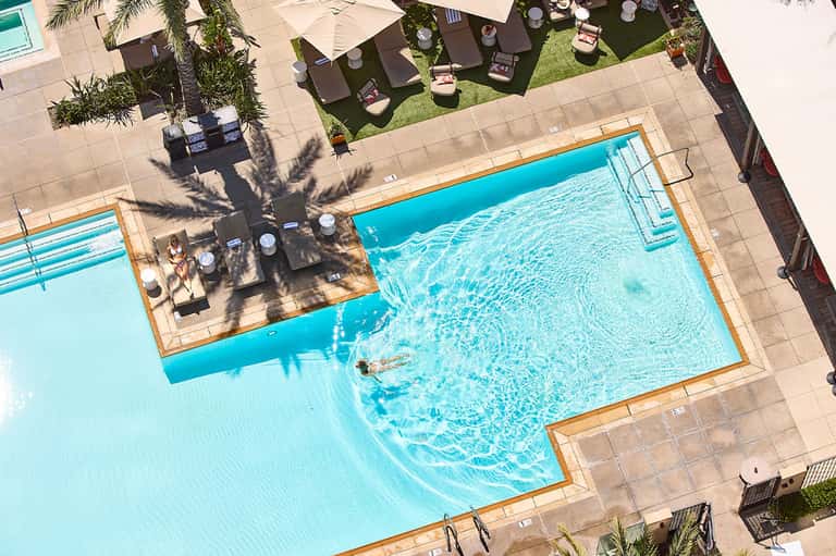 Overhead view of blue lap pool with spa, sun loungers, and palm tree shade