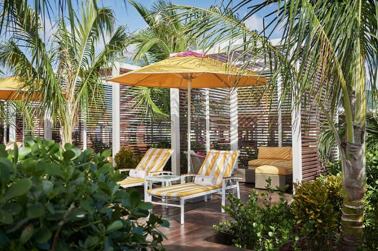 Shaded lounge area with yellow striped chairs, palm trees, and modern pergola structure