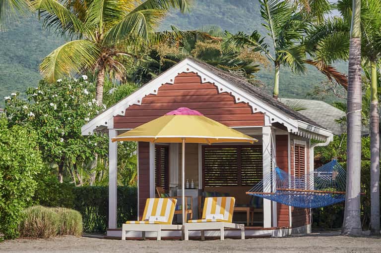 Tropical beachside cabana with red wood structure, yellow umbrella, and hammock with mountain views
