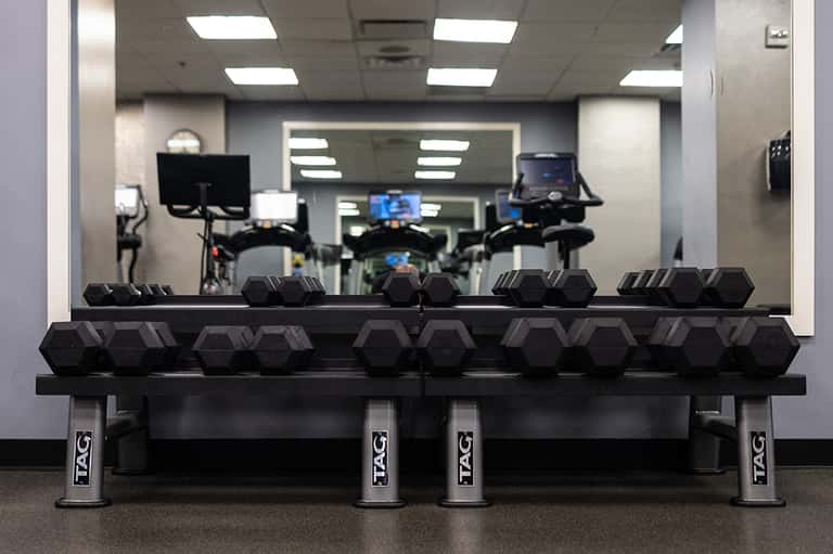 Fitness center with dumbbell racks and stationary bikes reflected in mirrors