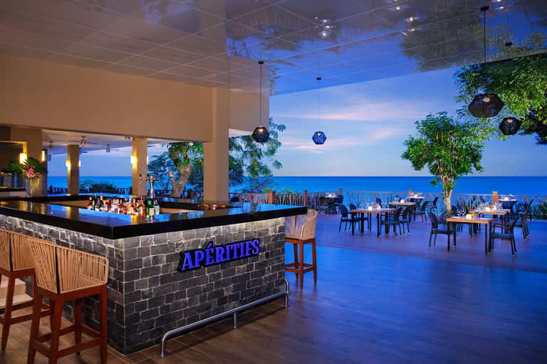 Oceanfront bar and dining area with blue lighting overlooking the sea at dusk