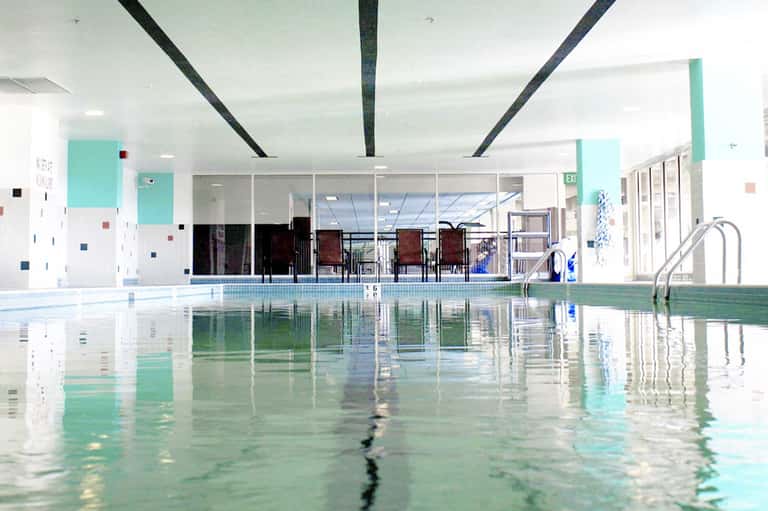 Indoor lap pool with turquoise water, white ceiling beams, and colorful accent walls in aquatic facility