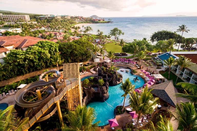 Aerial view of tropical resort with multiple pools, water slides, lush landscaping, and ocean