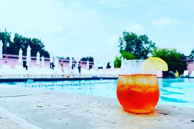 Red tropical cocktail with lime garnish on poolside, resort buildings and lap pool visible in background