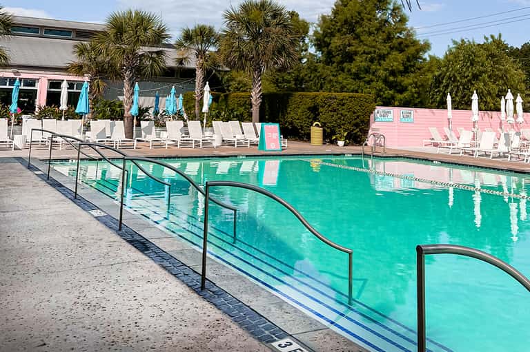 Turquoise swimming pool with lane dividers, white umbrellas, lounge chairs, and pink resort building