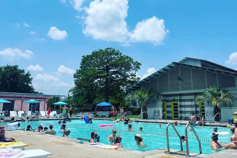Community swimming pool with lap lanes, umbrellas, changing facilities, and visitors
