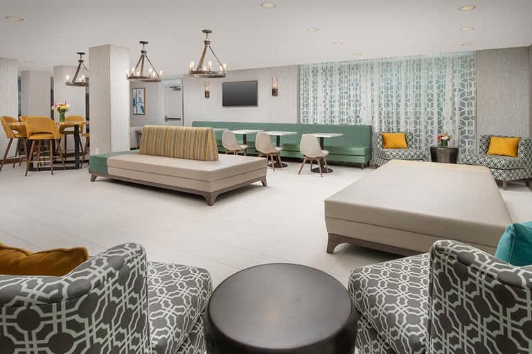Contemporary hotel lobby lounge with green sofa, patterned chairs, and pendant lighting