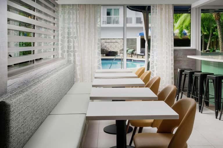 Resort dining area with window seating overlooking pool, featuring tan chairs and modern decor