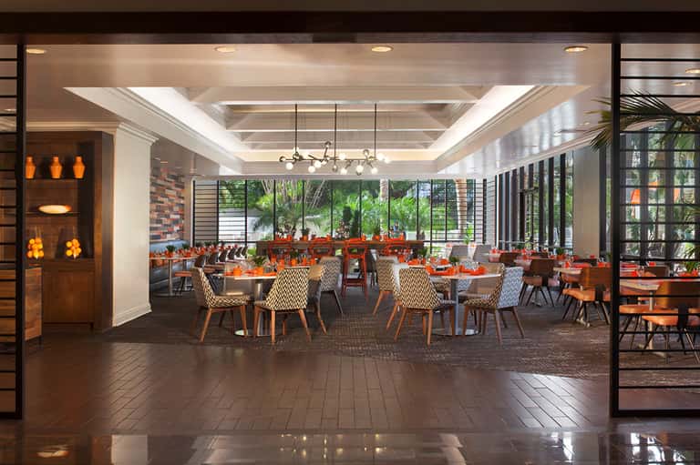 Modern hotel restaurant interior with tables, orange accents, and floor-to-ceiling windows