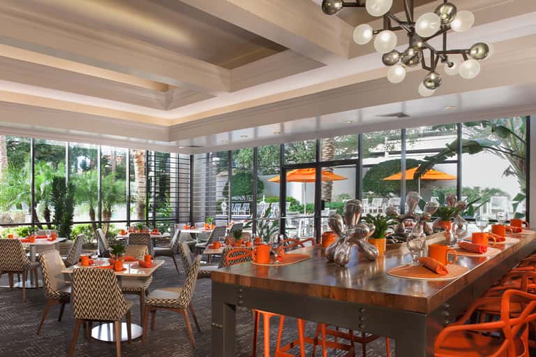 Elegant dining room with orange accents, modern lighting, and floor-to-ceiling windows
