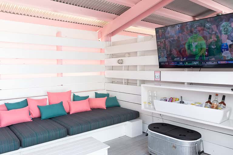Modern entertainment room with pink ceiling, teal and pink cushioned seating, and wall-mounted TV