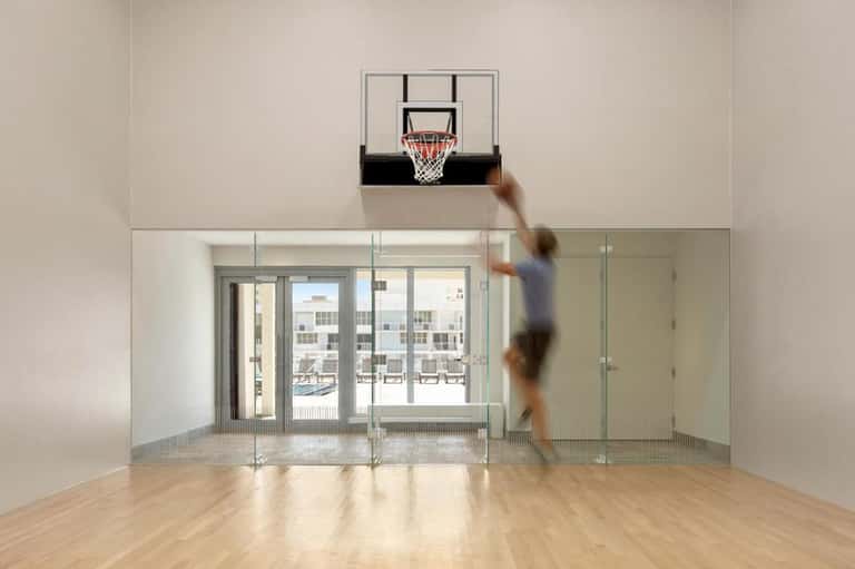 Empty resort gymnasium with basketball hoop, glass wall, and outdoor terrace access