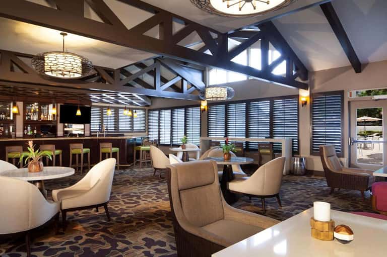 Upscale lounge bar with wooden beams, cream seating, shuttered windows, and ocean views