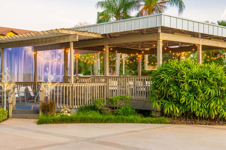 Covered resort patio with string lights, lounge chairs, views of palm trees and tropical vegetation
