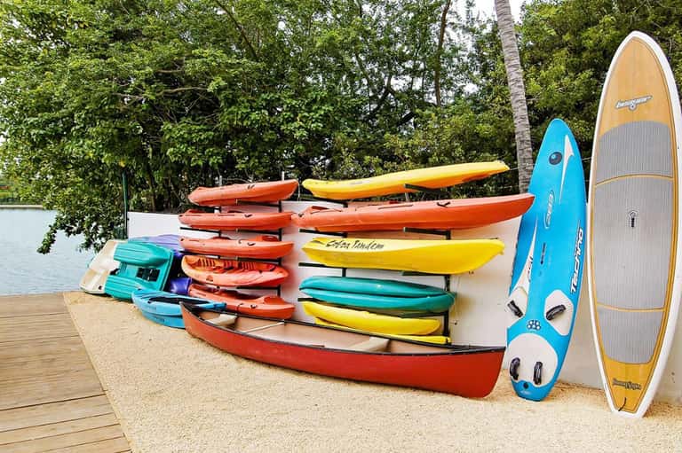 Colorful kayaks and paddleboards stacked on wooden dock with tropical water view