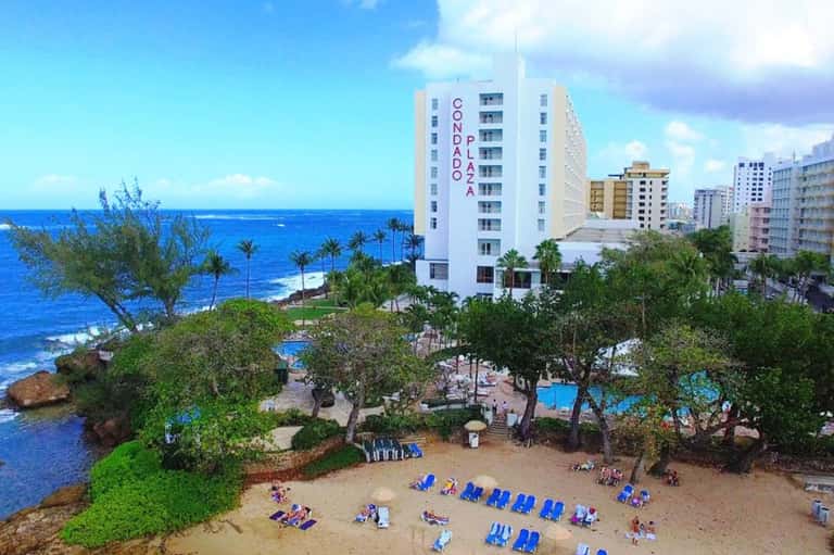 Beachfront hotel building overlooking rocky coastline and sandy beach with lounge chairs