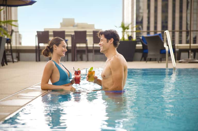 Couple enjoying cocktails in an urban rooftop pool with city skyline backdrop