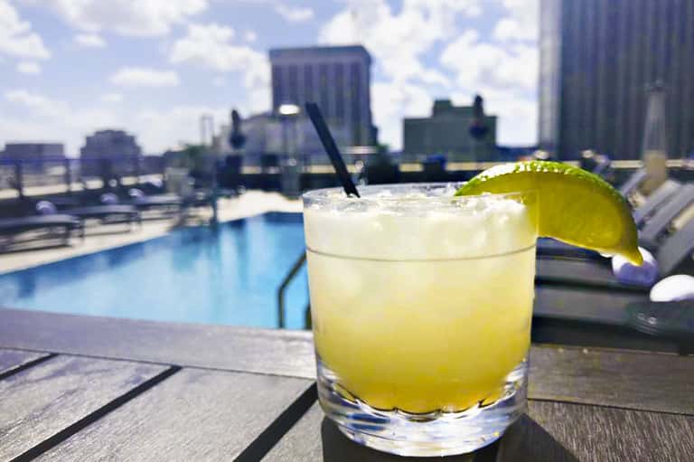 Citrus cocktail with lime wheel on rooftop bar overlooking city skyline and pool