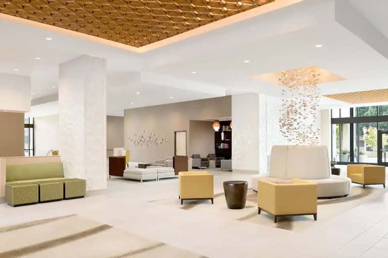 Spacious modern hotel lobby with white columns, textured ceiling details, comfortable seating, and contemporary design